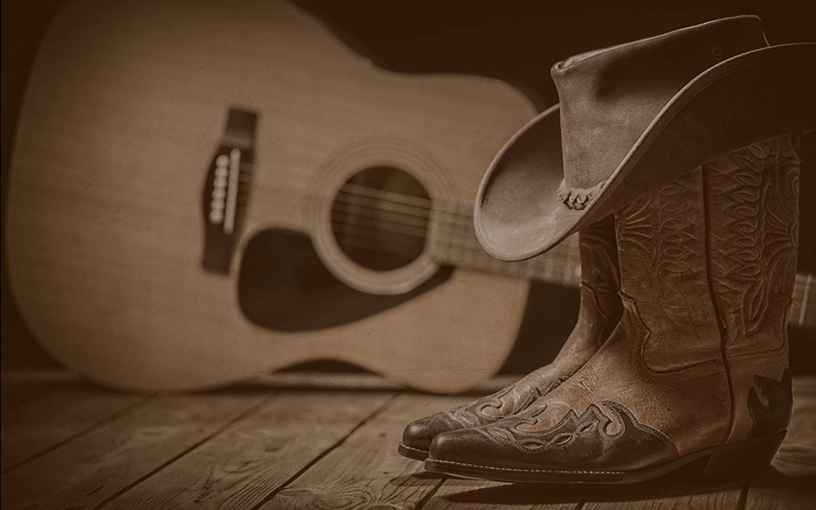 A guitar, cowboy boots, and cowboy hat in sepia tone.